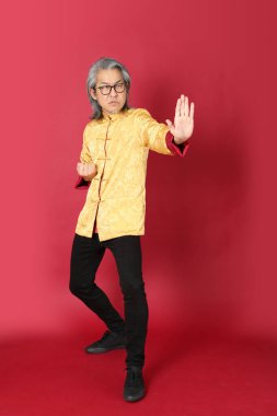 Kırmızı arka planda duran geleneksel altın rengi Çin elbiseleri giyen kıdemli Asyalı adam..