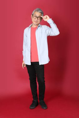 Kırmızı arka planda duran mavi tişörtlü, uzun saçlı kıdemli Asyalı adam..