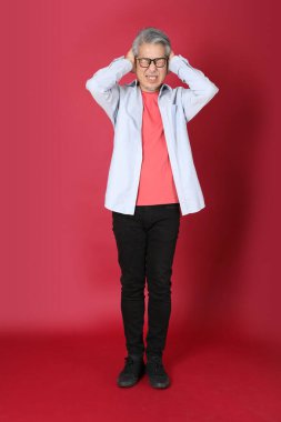 Kırmızı arka planda duran mavi tişörtlü, uzun saçlı kıdemli Asyalı adam..