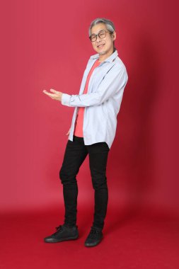 Kırmızı arka planda duran mavi tişörtlü, uzun saçlı kıdemli Asyalı adam..