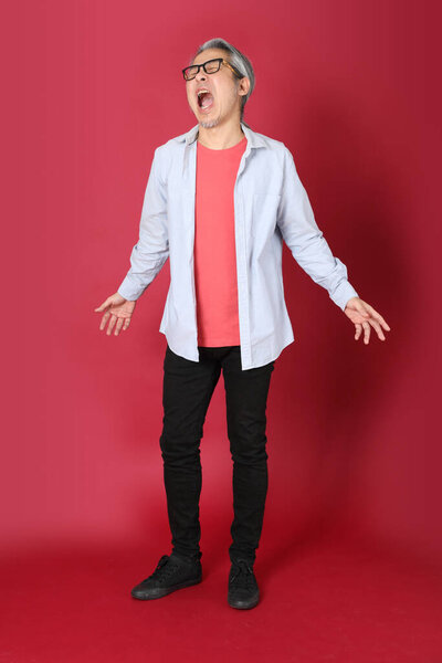 Старший азиат в голубой рубашке с длинными волосами стоит на красном фоне.