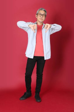 Kırmızı arka planda duran mavi tişörtlü, uzun saçlı kıdemli Asyalı adam..