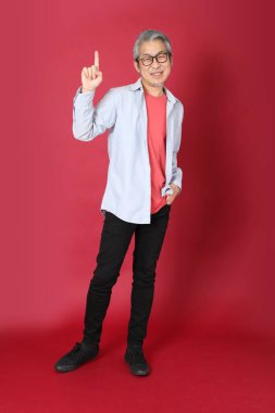 Kırmızı arka planda duran mavi tişörtlü, uzun saçlı kıdemli Asyalı adam..