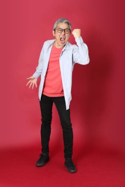 Kırmızı arka planda duran mavi tişörtlü, uzun saçlı kıdemli Asyalı adam..