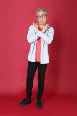 Kırmızı arka planda duran mavi tişörtlü, uzun saçlı kıdemli Asyalı adam..