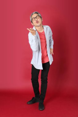 Kırmızı arka planda duran mavi tişörtlü, uzun saçlı kıdemli Asyalı adam..