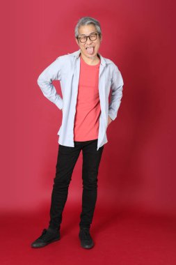 Kırmızı arka planda duran mavi tişörtlü, uzun saçlı kıdemli Asyalı adam..