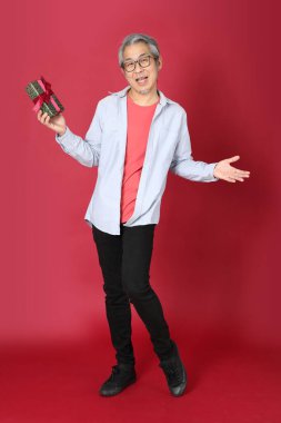 Kırmızı arka planda duran mavi tişörtlü, uzun saçlı kıdemli Asyalı adam..