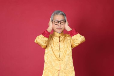 Kırmızı arka planda duran, Çin geleneği giyinmiş yaşlı Asyalı bir adamın portresi..