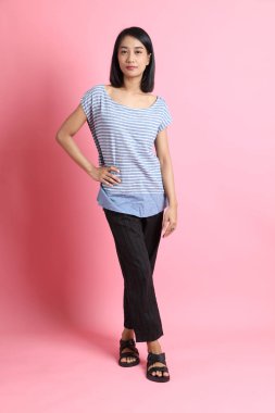 Pembe arka planda duran mavi gömlekli melez kadın..