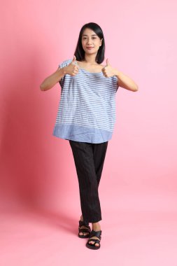 Pembe arka planda duran mavi gömlekli melez kadın..