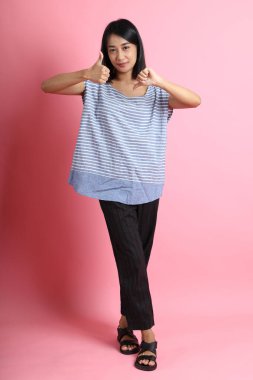 Pembe arka planda duran mavi gömlekli melez kadın..