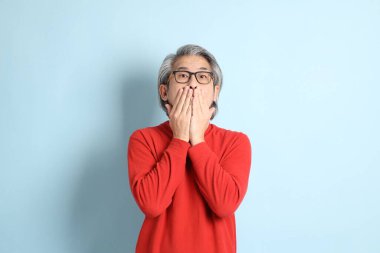 Mavi arka planda duran kıdemli Asyalı adam..