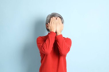 Mavi arka planda duran kıdemli Asyalı adam..