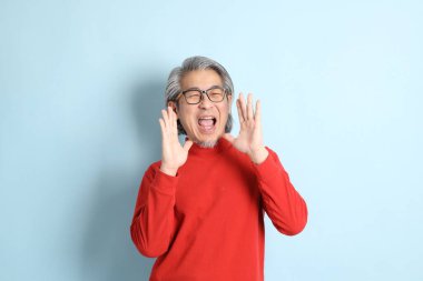 Mavi arka planda duran kıdemli Asyalı adam..