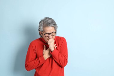 Mavi arka planda duran kıdemli Asyalı adam..