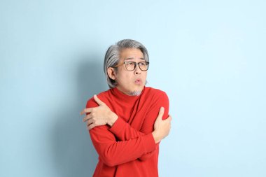 Mavi arka planda duran kıdemli Asyalı adam..