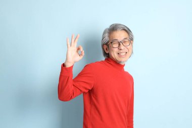 Mavi arka planda duran kıdemli Asyalı adam..