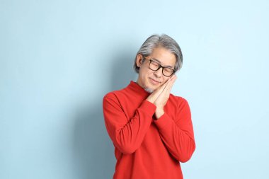 Mavi arka planda duran kıdemli Asyalı adam..