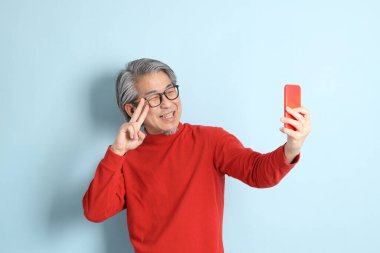 Mavi arka planda duran kıdemli Asyalı adam..