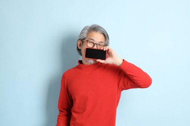 Mavi arka planda duran kıdemli Asyalı adam..