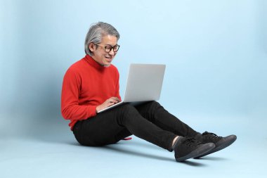 Mavi arka planda duran kıdemli Asyalı adam..