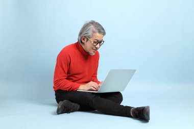 Mavi arka planda duran kıdemli Asyalı adam..