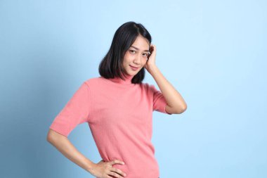 Mavi arka planda duran pembe elbiseli genç Asyalı kadın..