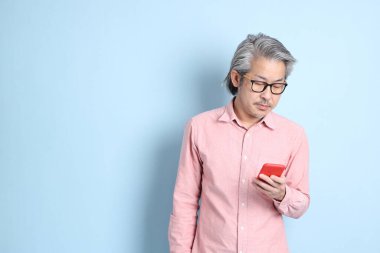 The senior Asian man standing on the blue background with pink shirt.