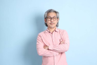 The senior Asian man standing on the blue background with pink shirt.