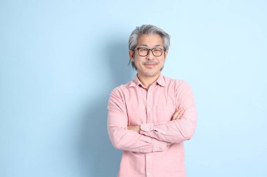 The senior Asian man standing on the blue background with pink shirt.