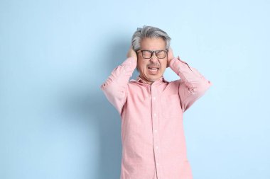 The senior Asian man standing on the blue background with pink shirt.