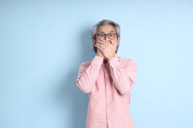 The senior Asian man standing on the blue background with pink shirt.