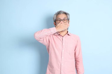 The senior Asian man standing on the blue background with pink shirt.