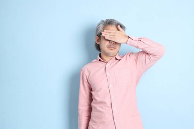The senior Asian man standing on the blue background with pink shirt.