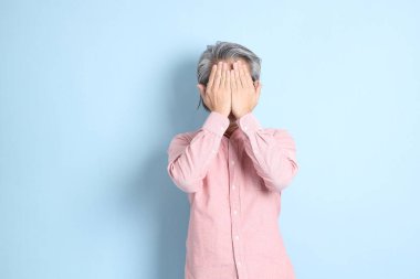 The senior Asian man standing on the blue background with pink shirt.