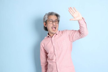 The senior Asian man standing on the blue background with pink shirt.