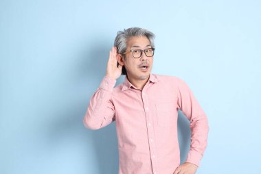 The senior Asian man standing on the blue background with pink shirt.