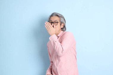 The senior Asian man standing on the blue background with pink shirt.