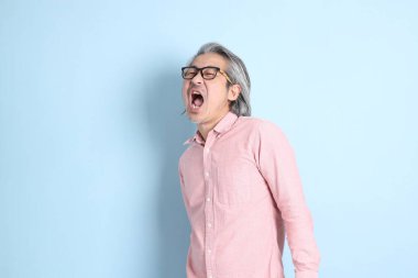 The senior Asian man standing on the blue background with pink shirt.