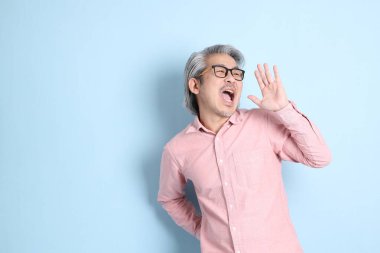 The senior Asian man standing on the blue background with pink shirt.