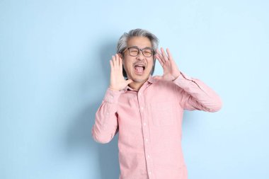 The senior Asian man standing on the blue background with pink shirt.