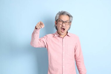 The senior Asian man standing on the blue background with pink shirt.
