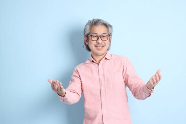 The senior Asian man standing on the blue background with pink shirt.