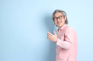 The senior Asian man standing on the blue background with pink shirt.