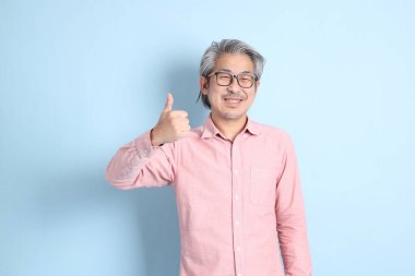 The senior Asian man standing on the blue background with pink shirt.