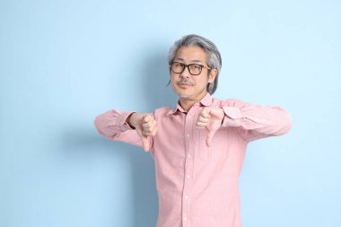 The senior Asian man standing on the blue background with pink shirt.
