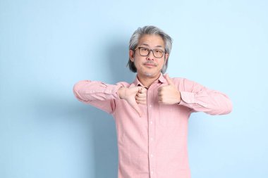 The senior Asian man standing on the blue background with pink shirt.
