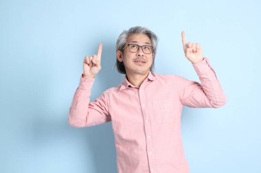 The senior Asian man standing on the blue background with pink shirt.