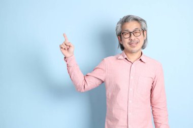 The senior Asian man standing on the blue background with pink shirt.